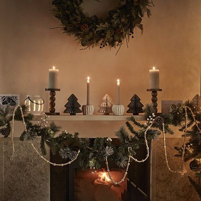 Mantelpiece with faux foliage, paper Christmas trees and candles. Shop Christmas decorations 