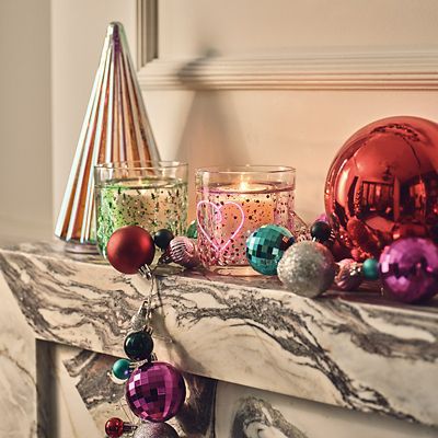 Mantelpiece with neon light-up candles and brightly coloured decorations. Shop Christmas decorations 