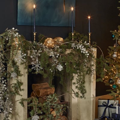 Mantelpiece with faux foliage, glittery decorations and tall candles. Shop Christmas decorations