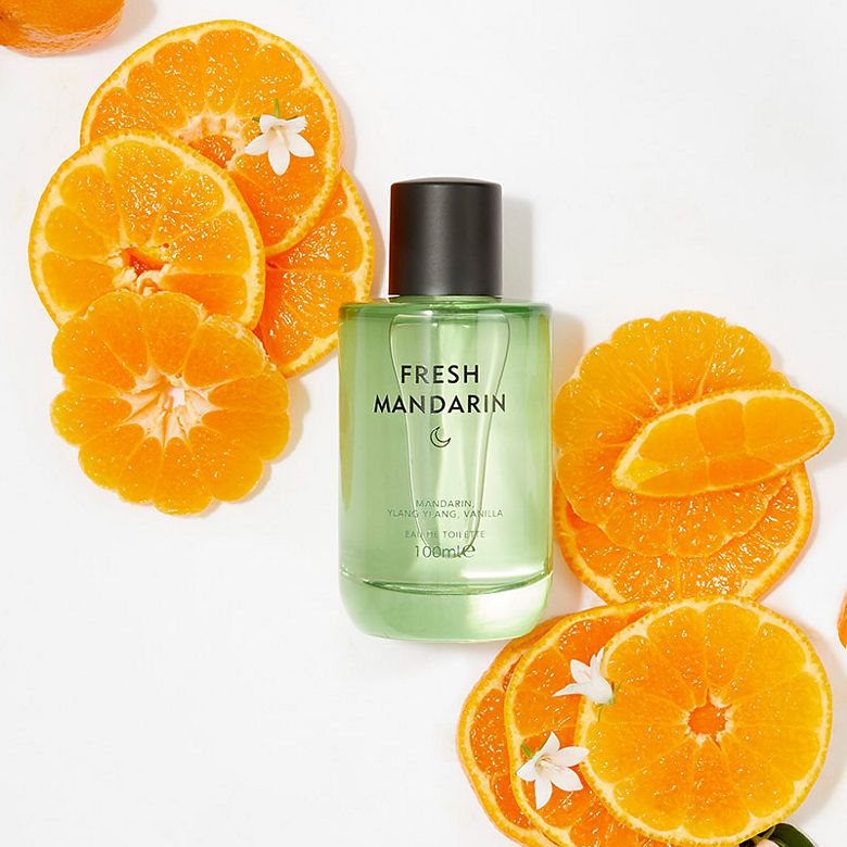 A bottle of Mandarin fragrance by Discover surrounded by oranges. Shop women’s perfume