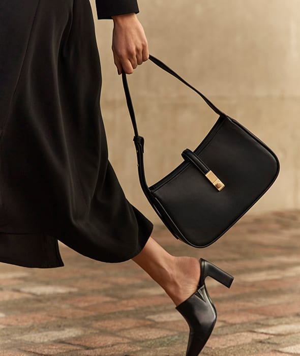 Woman wearing black dress, black shoes and carrying black bag. Shop women’s accessories