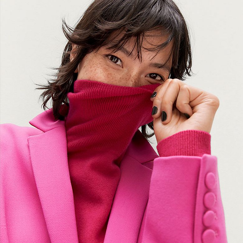 Woman wearing hot pink cashmere polo-neck jumper and pink blazer. Shop cashmere clothing and accessories 